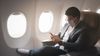 Man sitting on an airplane, wearing a medical face mask, looking at his mobile phone